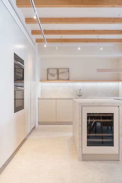 Architectural project - spacious kitchen, beige kitchen, home cooking, Japandi influence, white kitchen, built-in oven, recessed lighting, integrated appliances, open kitchen, under-cabinet lighting, wood, timber, natural light, inviting atmosphere, sustainable design, contemporary style, neutral tones, exposed beams, ceiling beams, functional space, beige, light wood, timber beams, neutral palette, eco-friendly materials, clean lines, white, cozy vibe, Nordic style, stone, bright kitchen, Scandinavian design, residential space, minimalist kitchen, modern kitchen, sleek design, kitchen island, minimal decor, modern interior, warm palette