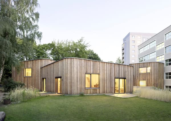 Architectural project - cozy interior, natural materials, wood, timber, glass, green, neutral tones, beige, light wood, low carbon design, daylight optimization, timber construction, honey wood, organic design, minimalist vibe, contemporary design, glass doors, sustainable building, wood panels, biophilic design, passive house, landscape integration, large windows, timber cladding, eco friendly home, inviting home, modern architecture, energy efficient, nature-inspired, garden view, wooden facade, residential building, simple lines, curved roof, suburban home, green space, minimal landscaping, urban context, warm lighting, sleek exterior, environmentally conscious, community housing, architectural harmony, urban garden, modern suburb