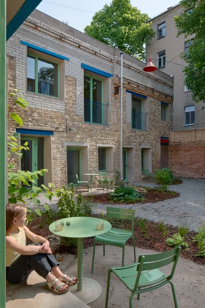 Architectural project - lush plants, rustic courtyard, cozy ambiance, exposed brick, vibrant accents, modern patio, historic building, urban courtyard, paving stones, residential courtyard, green furniture, courtyard garden, inviting courtyard, reclaimed brick, patio scene, city home, city oasis, outdoor nook, shady spot, eco courtyard, natural light, sustainable design, community space, daylight, multi-use space, concrete paving, compact space, contemporary touch, rustic charm, casual seating, social space, relaxed atmosphere, outdoor seating, adaptive reuse, rustic texture, cozy outdoor, outdoor gathering, brick facade, greenery, green design, outdoor retreat, eco renovation, sustainable renovation, urban garden, terrace garden, natural garden, mixed materials, outdoor relaxation, urban retreat, urban living, urban vibe