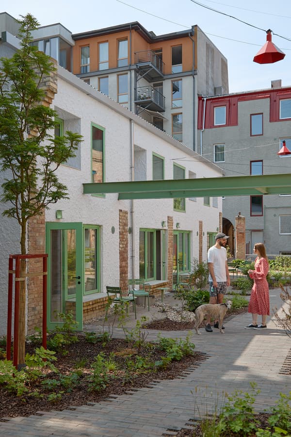 Architectural project - red accents, urban renewal, urban revitalization, vibrant community, mixed-use area, brickwork, roof terrace, urban texture, paved path, pastel green doors, white plaster, repurposed materials, eco district, green city, open-air living, shared garden, energy-efficient housing, neighborhood revitalization, city atmosphere, eco-friendly design, city living, cityscape, community space, sustainable architecture, green, urban oasis, contemporary design, social space, outdoor seating, color contrast, passive house, natural ventilation, modern facade, plaster, brick, greenery, modern living, light facade, urban garden, courtyard, daylight use, architectural contrast, connection to nature, residential block, mixed materials, urban housing, red