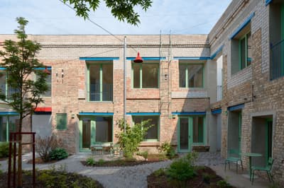 Architectural project - residential complex, blue accents, vintage style, exposed brick, plant life, outdoor furniture, refurbishment, historical building, teal accents, climbing plants, modern courtyard, shared courtyard, colorful frames, painted wood, folding chairs, inviting area, laid-back atmosphere, wood, metal, outdoor space, relaxed vibe, natural light, sustainable design, glass, warm tones, community space, green, neutral tones, beige, industrial style, blue, urban oasis, sunlight, industrial touch, adaptive reuse, tranquil setting, garden design, brick, eco friendly space, cozy corner, brick facade, red brick, natural environment, rustic exterior, garden seating, green space, urban garden, courtyard, renovation, mixed materials, red