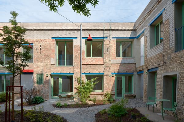 Architectural project - residential complex, blue accents, vintage style, exposed brick, plant life, outdoor furniture, refurbishment, historical building, teal accents, climbing plants, modern courtyard, shared courtyard, colorful frames, painted wood, folding chairs, inviting area, laid-back atmosphere, wood, metal, outdoor space, relaxed vibe, natural light, sustainable design, glass, warm tones, community space, green, neutral tones, beige, industrial style, blue, urban oasis, sunlight, industrial touch, adaptive reuse, tranquil setting, garden design, brick, eco friendly space, cozy corner, brick facade, red brick, natural environment, rustic exterior, garden seating, green space, urban garden, courtyard, renovation, mixed materials, red
