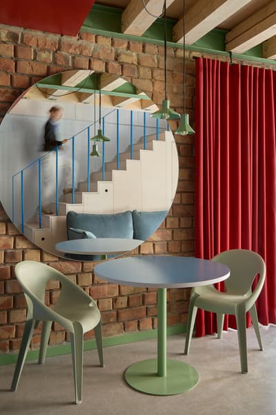 Architectural project - casual vibe, bold colors, industrial loft, artistic vibe, creative design, exposed brick, red curtains, vibrant interior, round mirror, pendant lamps, colorful chairs, green table, blue table, statement staircase, visible steps, eclectic decor, retro touch, unique elements, artistic influence, contemporary decor, circular mirror, sculptural elements, timber, green, ceiling beams, natural wood, multifunctional space, blue, casual seating, relaxed atmosphere, informal setting, industrial chic, modern rustic, timber ceiling, inviting interior, open plan, casual dining, brick, cozy corner, home office, concrete floor, open space, playful space, urban style, red