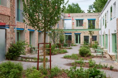 Architectural project - urban renewal, community garden, plant life, lively atmosphere, plants, outdoor furniture, shaded area, landscaping, brick walls, open courtyard, garden courtyard, teal accents, modern courtyard, red bricks, green doors, green window frames, patio chairs, greenery design, pedestrian space, vibrant environment, renovation project, historical facade, cheerful vibe, natural materials, outdoor living, sustainable design, warm tones, community space, contemporary architecture, urban oasis, rustic charm, public space, outdoor seating, adaptive reuse, pastel green, biophilic design, rustic finish, cozy vibe, social gathering, eco friendly space, brick facade, red brick, greenery, nature integration, garden path, urban garden, courtyard, exterior space, textured brick, brick building