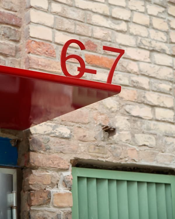 Architectural project - red accent, contrasting colors, brick wall, red canopy, red awning, number sign, modern signage, bold red, red number, street facade, exterior feature, colored metal, outdoor signage, numerical signage, red and green, exterior aesthetic, brick construction, street architecture, green gate, exterior combination, visual contrast, outdoor palette, cityscape detail, minimal design, architectural detail, urban landscape, contemporary style, green, industrial vibe, city architecture, beige, brown, building facade, industrial style, exterior detail, urban design, geometric design, industrial chic, clean lines, brick facade, outdoor design, facade design, modern exterior, urban facade, brick texture, red