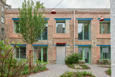Architectural project - balcony, urban dwelling, colorful facade, vibrant design, modern renovation, repurposed space, shared space, brickwork, exposed brick, industrial look, pendant lights, patio seating, landscaped garden, paving stones, courtyard view, city courtyard, recycled brick, city home, social housing, garden lights, green trim, colored windows, aluminum doors, metal doors, brick pathway, natural materials, natural light, sustainable design, reclaimed materials, eco design, community space, contemporary architecture, grey, green, daylight, industrial vibe, blue, outdoor seating, adaptive reuse, low carbon, large windows, energy efficient, brick facade, red brick, heritage building, greenery, natural environment, residential building, sustainable renovation, urban garden, urban facade, urban living, red