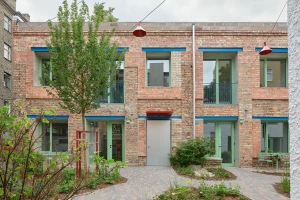 Architectural project - balcony, urban dwelling, colorful facade, vibrant design, modern renovation, repurposed space, shared space, brickwork, exposed brick, industrial look, pendant lights, patio seating, landscaped garden, paving stones, courtyard view, city courtyard, recycled brick, city home, social housing, garden lights, green trim, colored windows, aluminum doors, metal doors, brick pathway, natural materials, natural light, sustainable design, reclaimed materials, eco design, community space, contemporary architecture, grey, green, daylight, industrial vibe, blue, outdoor seating, adaptive reuse, low carbon, large windows, energy efficient, brick facade, red brick, heritage building, greenery, natural environment, residential building, sustainable renovation, urban garden, urban facade, urban living, red