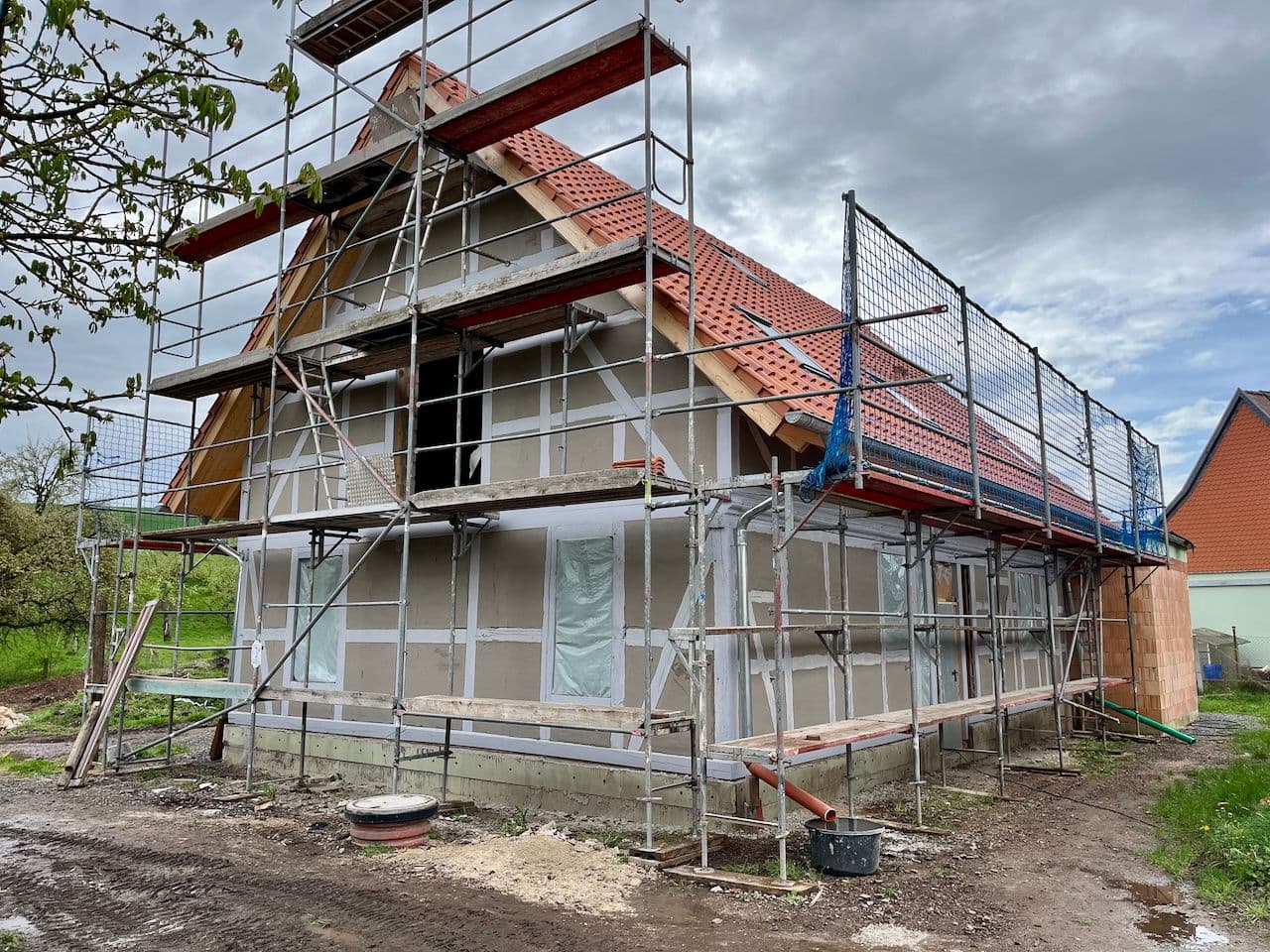 Architectural project - house renovation, energy-efficient home, exposed framework, terracotta roof, architectural renovation, exterior renovation, home build, natural materials, wood, timber, scaffolding, outdoor space, timber frame, passive design, modular construction, sustainable construction, grey, construction site, under construction, structural work, brown, concrete, low carbon design, exterior, building process, unfinished building, residential construction, eco-friendly materials, eco build, project site, plaster, pitched roof, terracotta, brick, gable roof, wooden structure, building envelope, home improvement, rural house, red