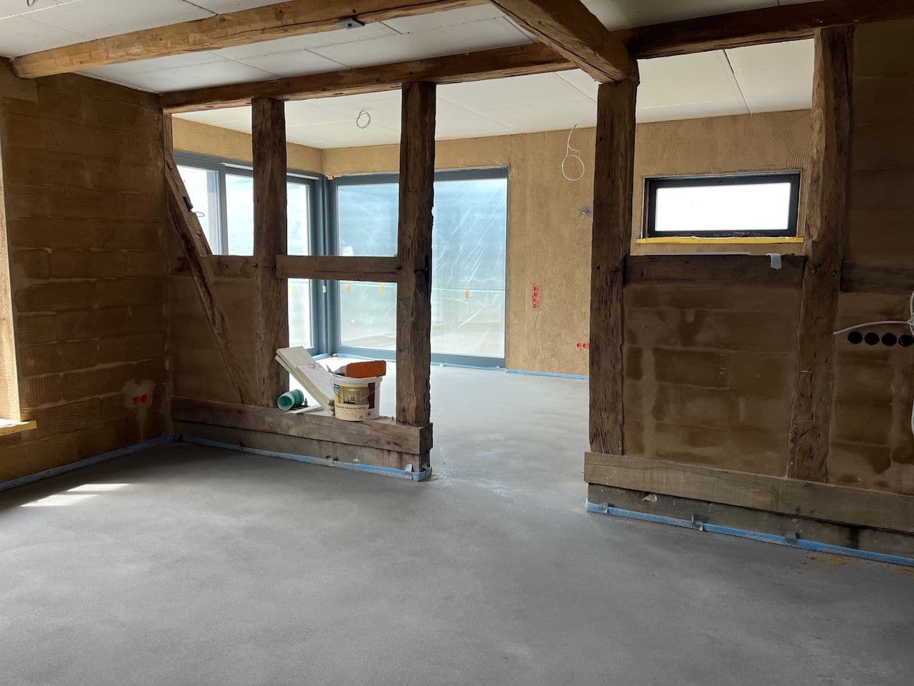 Architectural project - light grey, sustainable build, rustic feel, rustic structure, warm brown, unfinished walls, minimal design, natural materials, timber, raw materials, timber frame, natural light, warm tones, neutral tones, construction site, exposed beams, daylight, building site, beige, wood beams, rustic modern, adaptable space, structural wood, modern rustic, plaster, multifunctional room, interior, plaster walls, concrete floor, open space, eco renovation, natural insulation, bright room