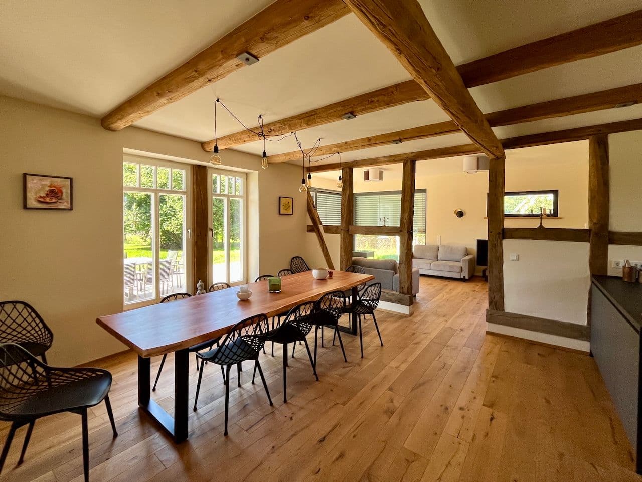 Architectural project - beige walls, living room, patio view, modern farmhouse, kitchen area, farmhouse table, rustic beams, retro influence, black accents, black chairs, warm interior, natural materials, wood, timber, metal, natural light, glass, eco design, exposed beams, daylight, light wood, simple design, honey wood, timber beams, neutral palette, relaxed atmosphere, glass doors, wood floor, earth tones, modern rustic, sustainable home, large windows, indoor outdoor, cozy vibe, timber ceiling, rustic style, open layout, open plan, living area, dining area, wooden table, dining table, inviting space, comfortable seating, family room, minimal decor, interior design, renovation, casual elegance, contemporary living, remodel
