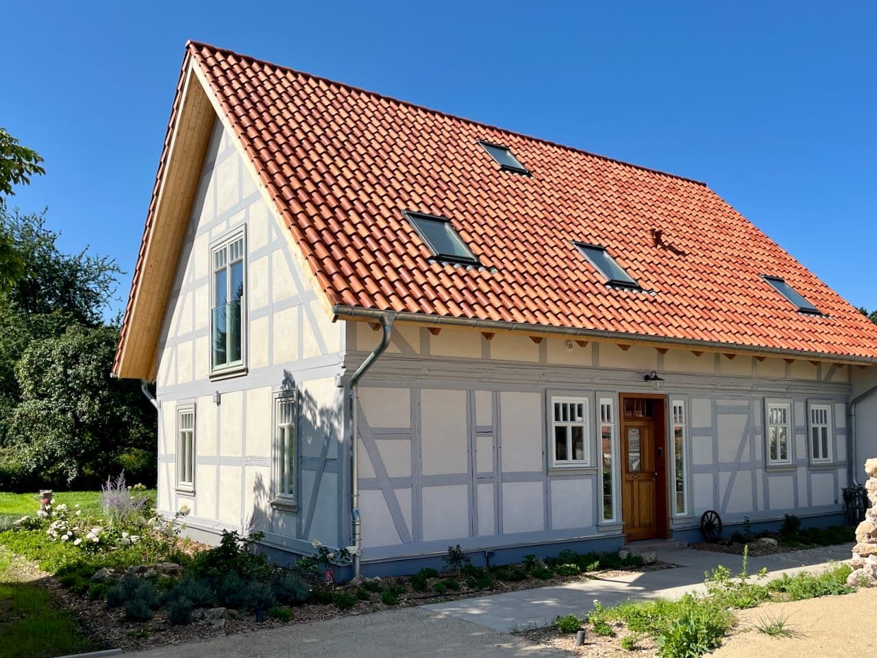 Architectural project - heritage design, skylights, terracotta roof, classic design, light blue accents, farmhouse aesthetic, natural materials, wood, timber, timber frame, glass, eco design, exposed beams, outdoor setting, beige, natural setting, rustic charm, exterior, sustainable home, scenic view, white facade, timber cladding, white, cozy vibe, timber house, rural home, countryside home, inviting entrance, airy space, pitched roof, traditional architecture, terracotta, tranquil environment, sunny day, garden view, wooden house, family home, residential building, cottage style, traditional house, country living, clay tiles, wooden door, red
