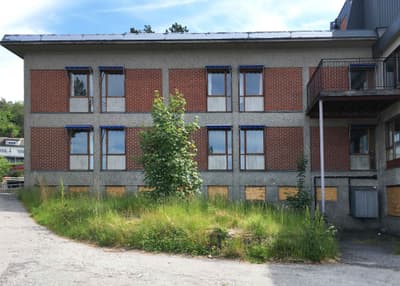 Architectural project - exposed concrete, exterior facade, educational facility, concrete facade, double-height windows, low-maintenance facade, mid-century style, robust structure, eco contrast, renovation potential, brick material, concrete material, sustainable potential, modernist touch, natural growth, landscaping, suburban feel, education use, urban setting, industrial design, raw materials, steel, metal, utilitarian design, outdoor space, warm tones, exposed structure, grey, green, neutral tones, industrial vibe, concrete, flat roof, simple design, adaptive reuse, adaptable space, large windows, rectangular windows, brick, brick facade, greenery, natural environment, exterior view, functional layout, urban architecture, educational space, school building, industrial building, educational architecture, practical design, urban vibe, red