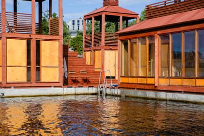 Architectural project - waterfront, floating structure, water reflection, houseboat, summer retreat, floating building, lakeside, reflective surfaces, boathouse, relaxed environment, warm woods, wood, timber, outdoor space, rustic touch, passive design, glass, natural tones, contemporary style, brown, timber facade, golden, modern design, outdoor leisure, serene space, orange, sustainable building, natural ventilation, large windows, glass walls, inviting space, peaceful vibe, wooden cladding, warm exterior, calm atmosphere, eco retreat, urban escape, open view, modern cabin, minimalist lines, warm palette, modern retreat