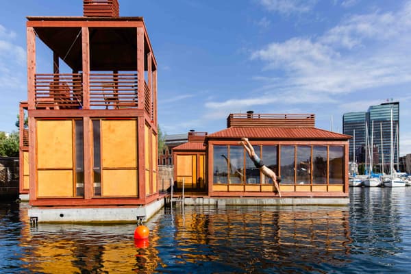 Architectural project - tiny house, eco living, city escape, waterfront, golden tones, deck area, water view, floating house, houseboat, water home, nautical design, minimal living, sustainable dwelling, private sanctuary, holiday home, seasonal home, glass enclosure, waterfront living, natural materials, wood, timber, outdoor space, summer house, natural light, passive design, glass, modular design, neutral tones, timber structure, lightweight design, daylight, brown, blue, eco friendly, glass panels, orange, warm wood, exposed wood, open plan, nature integration, wooden facade, compact living, modern retreat, urban retreat
