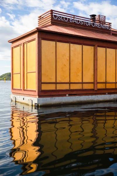 Architectural project - compact structure, water reflection, floating sauna, waterfront design, water sauna, aquatic architecture, lake sauna, Scandi design, floating building, traditional elements, wellness space, natural materials, wood, timber, natural light, sustainable design, warm tones, timber structure, beige, wood facade, golden, eco friendly, recreational space, wellness design, urban oasis, rustic charm, contemporary design, minimalist design, modern rustic, timber cladding, Nordic style, wooden roof, cozy atmosphere, tranquil environment, serene setting, reflective surface, wooden panels, outdoor retreat, sky view, simple lines, natural surroundings, urban retreat