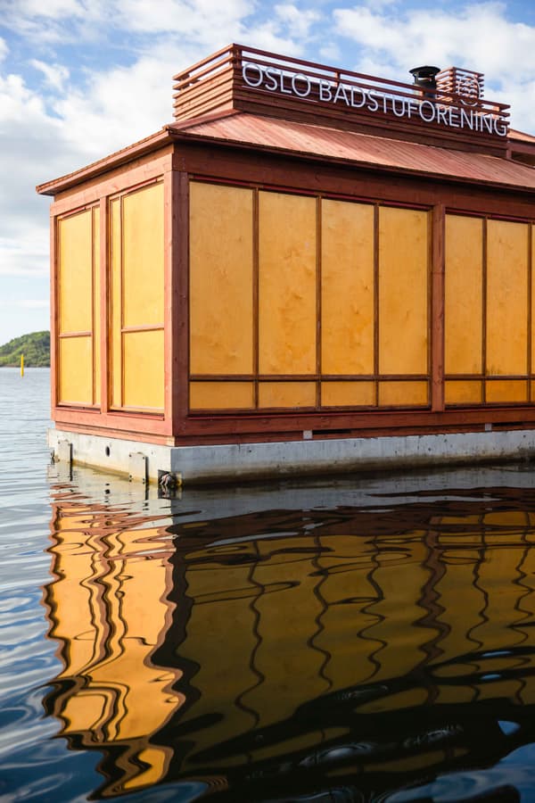 Architectural project - compact structure, water reflection, floating sauna, waterfront design, water sauna, aquatic architecture, lake sauna, Scandi design, floating building, traditional elements, wellness space, natural materials, wood, timber, natural light, sustainable design, warm tones, timber structure, beige, wood facade, golden, eco friendly, recreational space, wellness design, urban oasis, rustic charm, contemporary design, minimalist design, modern rustic, timber cladding, Nordic style, wooden roof, cozy atmosphere, tranquil environment, serene setting, reflective surface, wooden panels, outdoor retreat, sky view, simple lines, natural surroundings, urban retreat