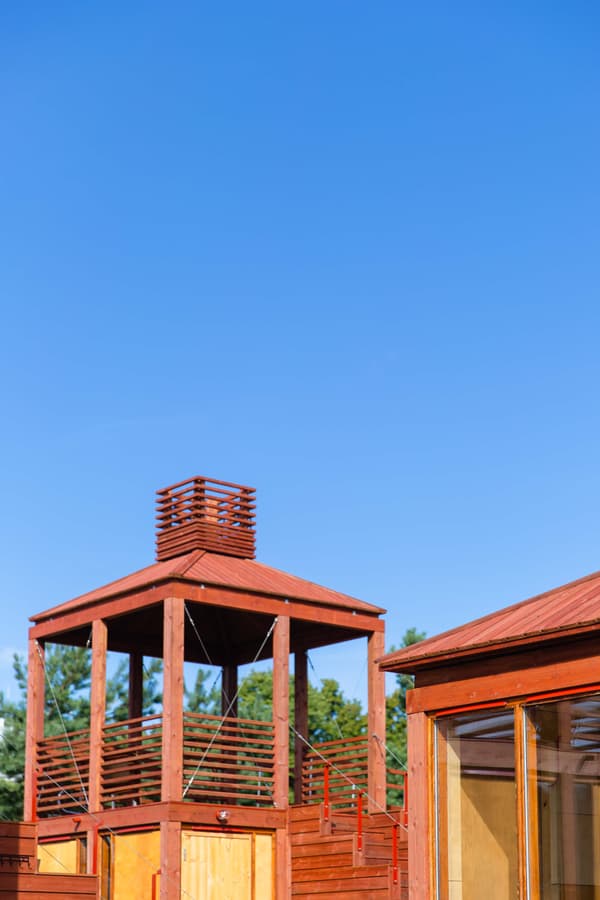 Architectural project - countryside escape, garden architecture, airy structure, garden pavilion, natural elements, countryside style, wooden pergola, red gazebo, wooden gazebo, terrace shelter, garden structure, red tones, wood plank design, shaded area, lawn feature, gathering spot, informal structure, weekend house, bright blue sky, wood, timber, wooden frame, outdoor living, exposed structure, sustainable architecture, timber structure, brown, natural wood, open air design, eco structure, rustic vibe, timber beams, leisure space, minimal structure, outdoor pavilion, rustic style, earthy tones, warm atmosphere, backyard feature, relaxing space, garden retreat, sunny day, garden view, wooden slats, outdoor retreat, architectural feature, red