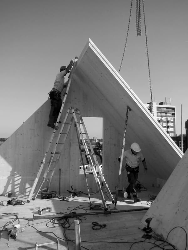 Architectural project - wood, timber, modular construction, neutral tones, construction phase, timber structure, structural timber, construction site, construction workers, modern construction, plywood, urban development, site safety, construction equipment, building site, structural design, engineered wood, wood beams, contemporary design, wood structure, plywood panels, prefabricated elements, white, modern architecture, architectural process, rooftop construction, standing seam, roof assembly, modern roofing, installation phase, roof frame, architectural innovation, building innovation, urban backdrop, cityscape view, black and white, building industry, architectural element