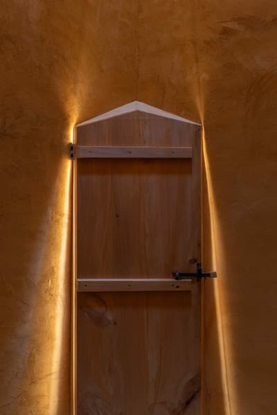Architectural project - ambient light, serene ambiance, private sanctuary, mood lighting, arched door, rustic entrance, golden hues, handcrafted door, safe haven, sheltering light, warm interior, intimate space, natural materials, architectural detail, wood, timber, sustainable design, warm tones, natural wood, low carbon design, eco friendly, organic design, rustic charm, minimalist style, earth tones, textured wall, plaster wall, inviting entrance, plaster, wood texture, rustic style, artisanal craftsmanship, cozy atmosphere, Mediterranean vibe, wooden structure, interior design, wooden door