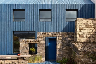 Architectural project - natural stone, harmony with nature, blue facade, ribbed texture, blue house, blue building, stone structure, geometric windows, minimalist windows, countryside charm, stone garden, rustic courtyard, modern entrance, vernacular elements, traditional meets modern, outdoor wall, blue decor, stone detailing, house exterior, rustic contemporary, sensory texture, nature-inspired design, outdoor space, rustic touch, passive design, sustainable design, grey, blue, rural architecture, contemporary design, eco materials, eco-friendly materials, modern rustic, landscape integration, energy efficient, stone, stone wall, rural vibe, residential building, contemporary house, textured facade, vertical cladding, modern rural, facade design, modern exterior, architectural contrast, rural retreat, muted tones, exterior cladding