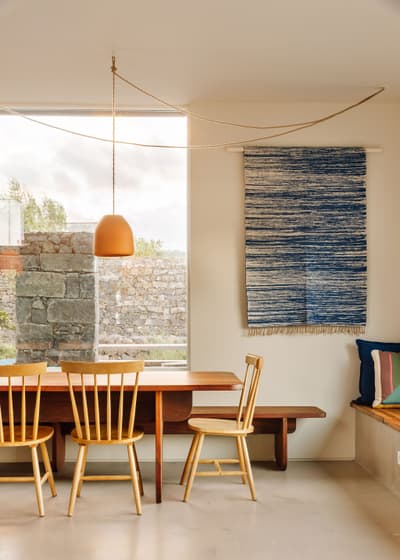 Architectural project - light-filled space, blue decor, home comfort, dining room, modern dining, wall hanging, wooden chairs, dining chairs, family dining, natural light, rustic touch, neutral tones, daylight, beige, light wood, blue, eco friendly, simple design, Scandinavian style, minimalist style, natural material, sustainable home, contemporary home, clean lines, indoor outdoor, harmonious design, cozy vibe, large window, dining area, wooden table, dining table, inviting space, earthy tones, warm atmosphere, casual dining, stone wall, tranquil vibe, comfortable seating, modern home, home design, interior design, relaxed space, warm lighting, calm setting, modern interior, pendant lamp, woven art