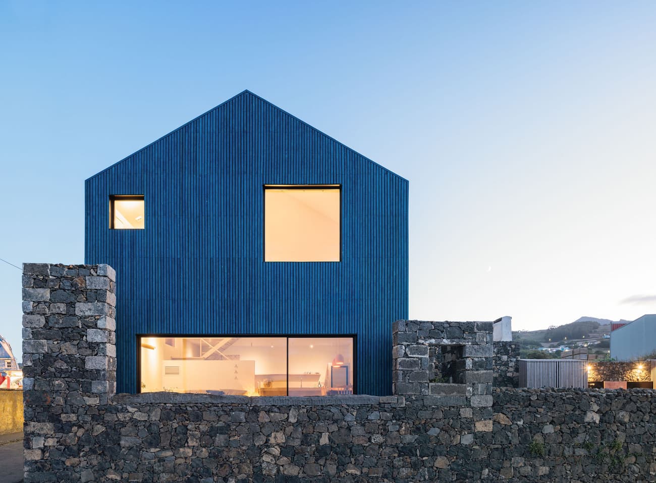 Architectural project - natural stone, clean architecture, harmony with nature, exposed stone, minimalist house, blue cladding, basalt stone, landscape, horizontal windows, blue facade, uniform color, rural landscape, open surroundings, contrast materials, architectural clarity, basalt, passive solar design, natural light, sustainable design, glass, grey, blue, eco friendly, natural setting, peaceful setting, minimalist architecture, contemporary design, large windows, countryside home, outdoor view, energy efficient, stone wall, quiet retreat, rural setting, barn style, residential building, textured facade, sleek design, home design, modern rural, simple lines, modern exterior, glass facade, rural house, picture window, modern house, geometric form