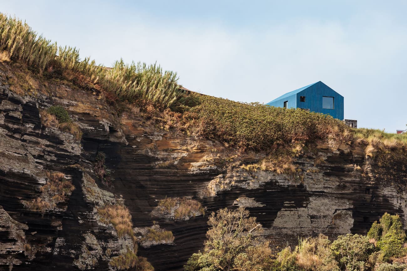 Architectural project - isolated home, picturesque location, natural scenery, cliff house, blue cabin, angular architecture, rugged landscape, coastal home, remote house, dramatic setting, outdoor escape, hillside structure, bold design, architectural statement, vernacular inspiration, rugged terrain, unique silhouette, striking design, coastal architecture, innovative home, blue exterior, contemporary style, landscape architecture, rustic charm, minimalist design, color contrast, tranquil setting, eco-friendly materials, scenic view, modern architecture, nature retreat, nature integration, off-grid living, nature immersion, reflective surface, vacation home, eco retreat, earthy textures, nature blend, landscape harmony, low impact design, sustainable living, modern cabin, modern retreat