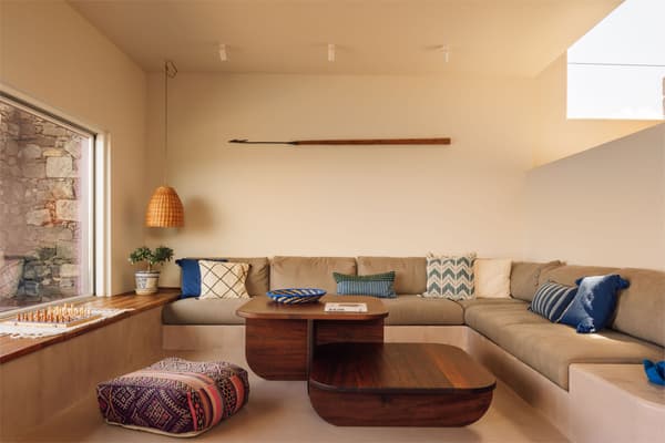 Architectural project - beige walls, lounging area, home comfort, corner sofa, wooden coffee table, woven pendant, boho chic, patterned cushions, decorative throw, pouf, chess board, tranquil ambiance, woven textures, indoor space, natural materials, relaxed vibe, natural light, bohemian style, warm tones, beige, brown, blue, sunlight, intimate setting, casual setting, neutral palette, minimalist design, relaxation spot, soft textures, modern rustic, inviting home, family space, earthy tones, Mediterranean style, cozy atmosphere, comfortable seating, bright interior, built-in seating, minimal decor, cozy living room, contemporary living