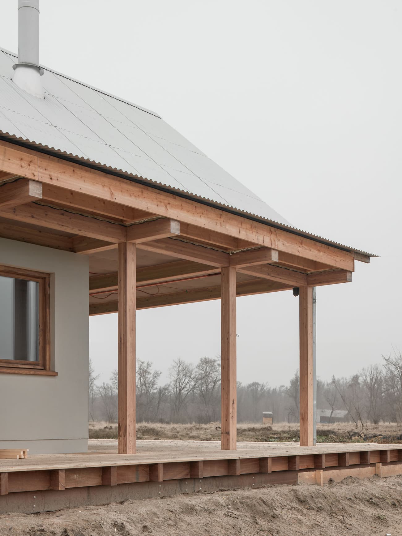Architectural project - modern farmhouse, quiet setting, veranda, natural materials, wood, metal, outdoor space, outdoor living, passive design, sustainable design, warm tones, corrugated roof, grey, neutral tones, structural timber, beige, brown, wood facade, timber facade, natural wood, rural architecture, simple design, serene atmosphere, minimalist architecture, minimalist design, eco materials, wood structure, modern rustic, open landscape, eco home, natural ventilation, metal roof, clean lines, timber cladding, wood cladding, timber house, countryside home, landscape view, pitched roof, rural setting, exterior view, country vibe, earthy palette, gabled roof, inviting exterior, rural house