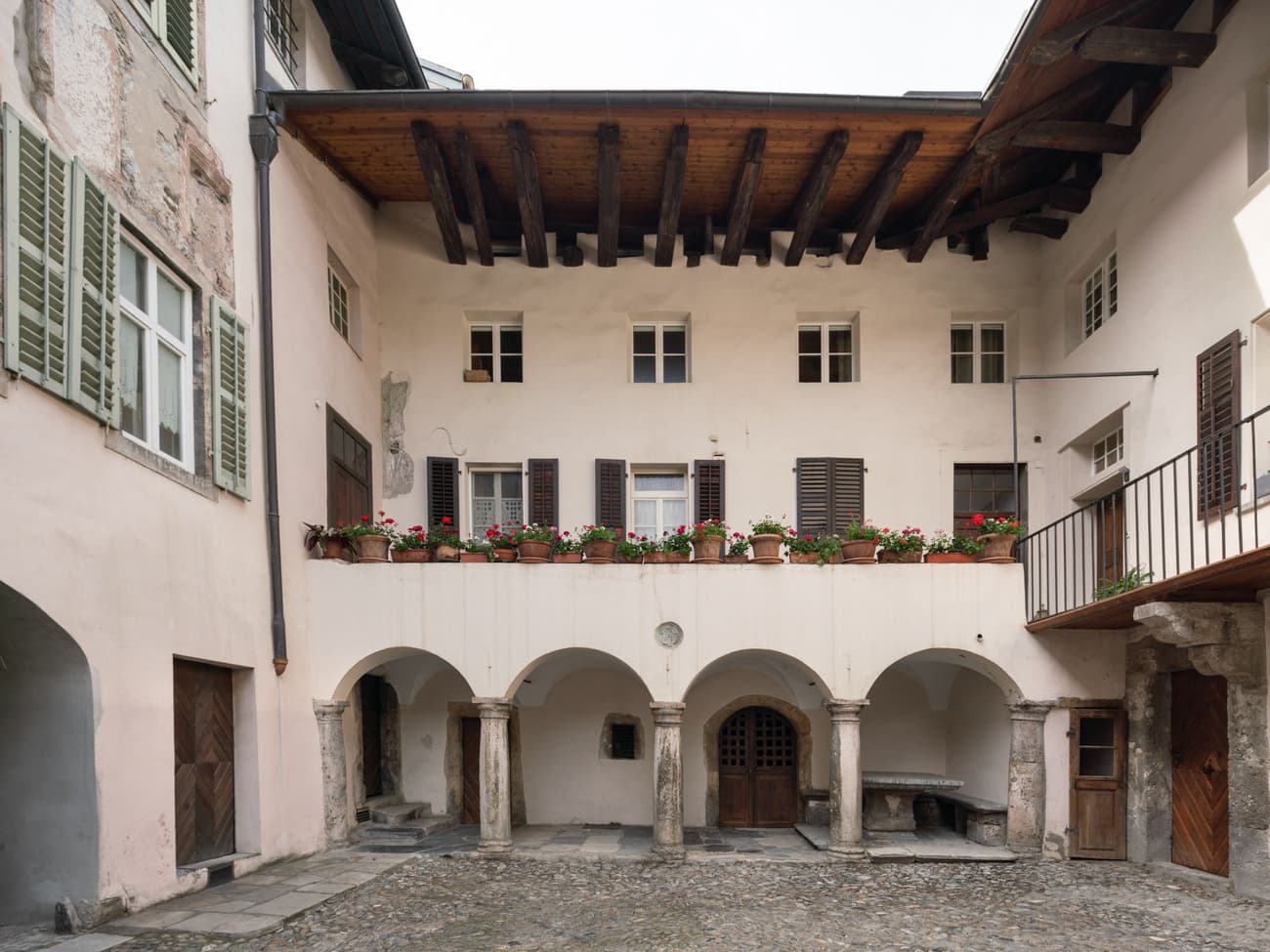 Architectural project - wooden shutters, rustic elegance, terracotta pots, period architecture, cultural heritage, old-world charm, residential courtyard, Southern European, classic design, traditional materials, vintage charm, traditional facade, outdoor courtyard, historic courtyard, courtyard architecture, arched colonnade, stone arches, stone pavement, cobblestone courtyard, villa courtyard, balcony details, flower pots, heritage restoration, wood, warm tones, neutral tones, exposed beams, beige, brown, wooden beams, natural textures, rustic charm, simple elegance, white, stone, plaster, inviting space, earthy tones, warm atmosphere, Mediterranean style, cozy outdoor, terracotta, classic architecture, heritage building, timeless design, plaster walls, exterior space