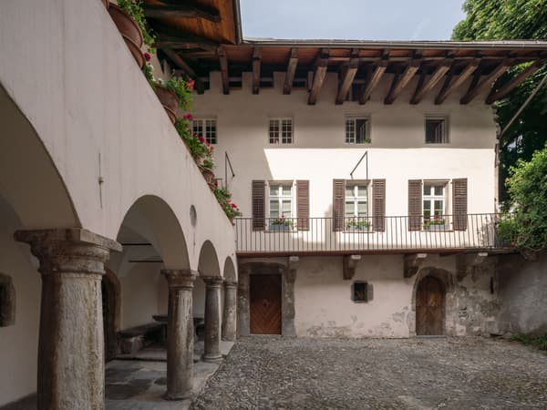 Architectural project - wooden shutters, rustic courtyard, rustic elegance, shaded area, historical charm, historic preservation, architectural heritage, traditional materials, countryside feel, stone paving, classic style, wooden balcony, historic courtyard, stone columns, arched walkway, vintage architecture, weathered textures, garden pots, window boxes, floral decor, ivy accents, tranquil courtyard, rural ambiance, stucco walls, rustic details, heritage garden, conservation architecture, natural materials, wood, outdoor space, outdoor living, natural tones, beige, brown, rustic charm, earth tones, white, stone, plaster, traditional design, rustic facade, heritage building, Mediterranean vibe, serene setting, rustic aesthetic, timeless design, wooden door, stone texture