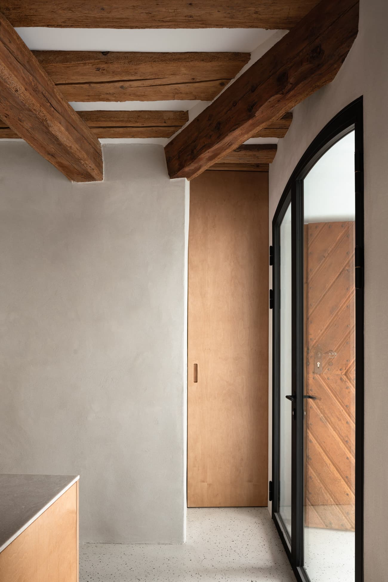 Architectural project - rustic interior, entrance, interior door, arched window, black accents, smooth plaster, black framed window, contemporary upgrades, heritage blend, Scandinavian vibes, natural materials, architectural detail, eco-friendly design, wood, timber, raw materials, metal, natural light, glass, warm tones, neutral tones, exposed beams, daylight, beige, brown, light wood, functional design, wood beams, timber beams, rustic charm, minimalist design, cozy space, modern rustic, clean lines, Nordic design, textured wall, plaster wall, plaster, rustic warmth, inviting space, glass door, earthy textures, sustainable interior, renovation, hallway, wooden door, entryway, remodel