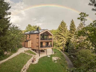 Architectural project - balcony, rural escape, nature getaway, rustic elegance, earthy, relaxing vibe, veranda, nature views, woodland home, treehouse vibe, tranquil, natural materials, wood, timber, natural light, outdoor living, passive design, glass, warm tones, green, neutral tones, beige, brown, light wood, natural setting, green architecture, metal roof, cozy atmosphere, forest retreat, eco cabin, sustainable cabin, forest house, wooden facade, timber exterior, gabled roof, steep roof, country home