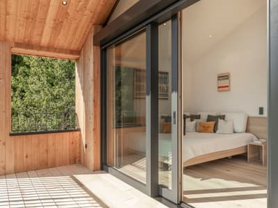 Architectural project - balcony, exposed timber, mountain retreat, contemporary cabin, modern decor, green view, balcony view, simple bed, timber terrace, cozy interior, warm interior, intimate space, natural materials, wood, timber, natural light, rustic touch, glass, warm tones, eco design, neutral tones, daylight, beige, brown, light wood, rustic modern, retreat space, indoor retreat, minimalist design, light tones, timber walls, modern rustic, sustainable home, nature view, indoor outdoor, white, Nordic style, large window, wood cabin, timber cabin, cozy cabin, residential design, tranquil vibe, relaxing space, wooden flooring, Scandinavian design, bright space, outdoor retreat, modern cabin, sliding glass doors