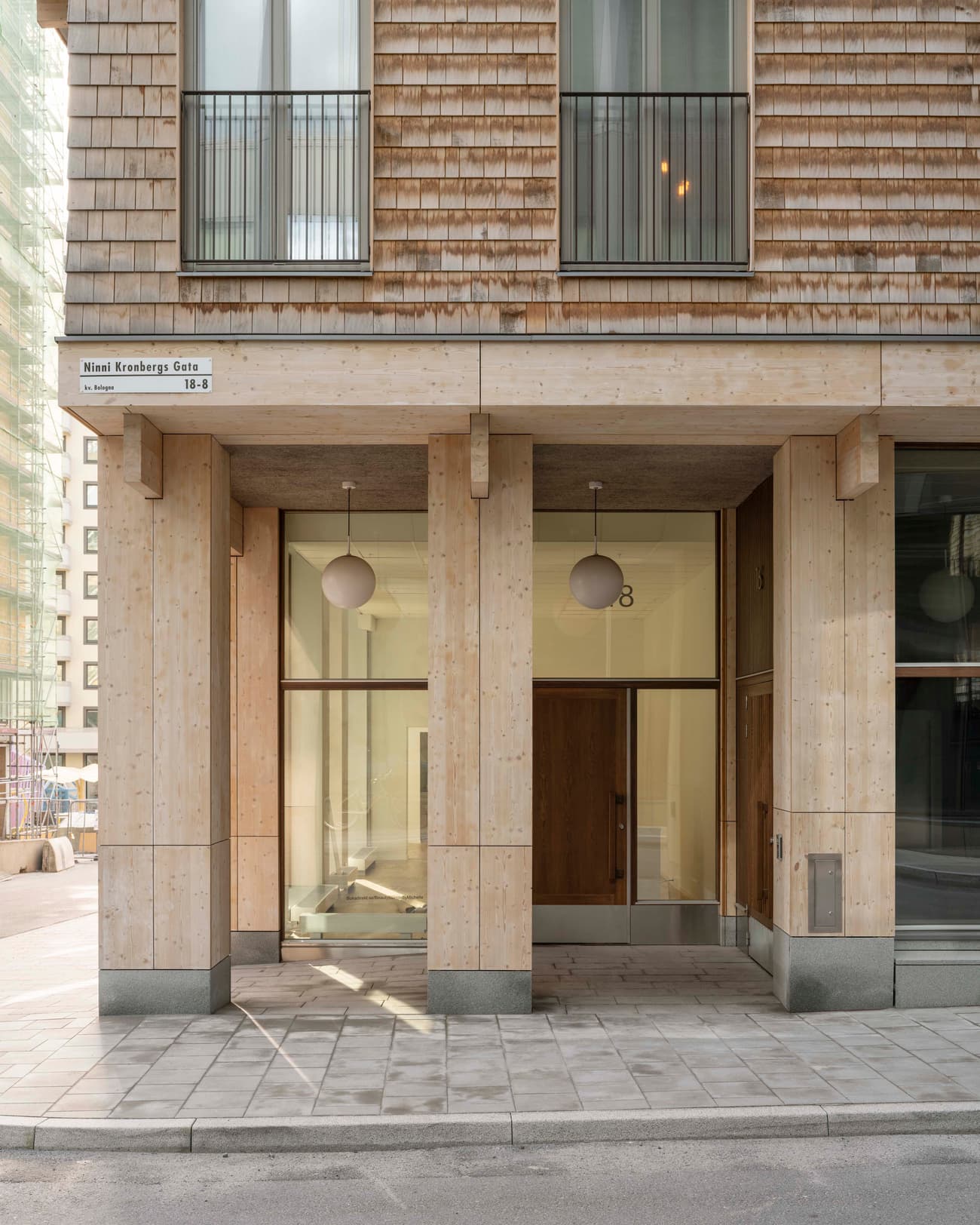 Architectural project - urban building, geometric lines, vertical lines, bright facade, grid pattern, mixed-use building, natural materials, architectural detail, sustainable materials, wood, timber, passive design, glass, warm tones, eco design, grey, neutral tones, city architecture, beige, concrete, wood facade, light wood, daylight optimization, Scandinavian style, minimalist design, glass doors, low carbon, modern facade, clean lines, large windows, simple elegance, Nordic design, energy efficient, inviting entrance, natural texture, environmental design, timber exterior, shingle cladding, warm exterior, pale wood, glass facade, structural rhythm, urban facade, urban style, urban modern, contemporary building