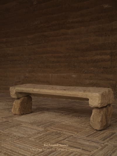 Architectural project - sustainability, natural stone, natural hues, rustic outdoor, rustic bench, stone bench, rugged texture, organic feel, rough finish, simple seating, courtyard seating, outdoor courtyard, versatile seating, weathered stone, garden bench, patio bench, primitive style, fired earth, raw materials, sustainable design, reclaimed materials, warm tones, beige, brown, eco friendly, compact space, natural setting, rustic charm, neutral palette, minimalist design, peaceful ambiance, earthy texture, rustic style, earthy tones, Mediterranean style, rural setting, tranquility, outdoor relaxation, outdoor bench, stone texture