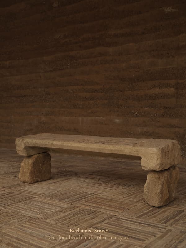 Architectural project - sustainability, natural stone, natural hues, rustic outdoor, rustic bench, stone bench, rugged texture, organic feel, rough finish, simple seating, courtyard seating, outdoor courtyard, versatile seating, weathered stone, garden bench, patio bench, primitive style, fired earth, raw materials, sustainable design, reclaimed materials, warm tones, beige, brown, eco friendly, compact space, natural setting, rustic charm, neutral palette, minimalist design, peaceful ambiance, earthy texture, rustic style, earthy tones, Mediterranean style, rural setting, tranquility, outdoor relaxation, outdoor bench, stone texture