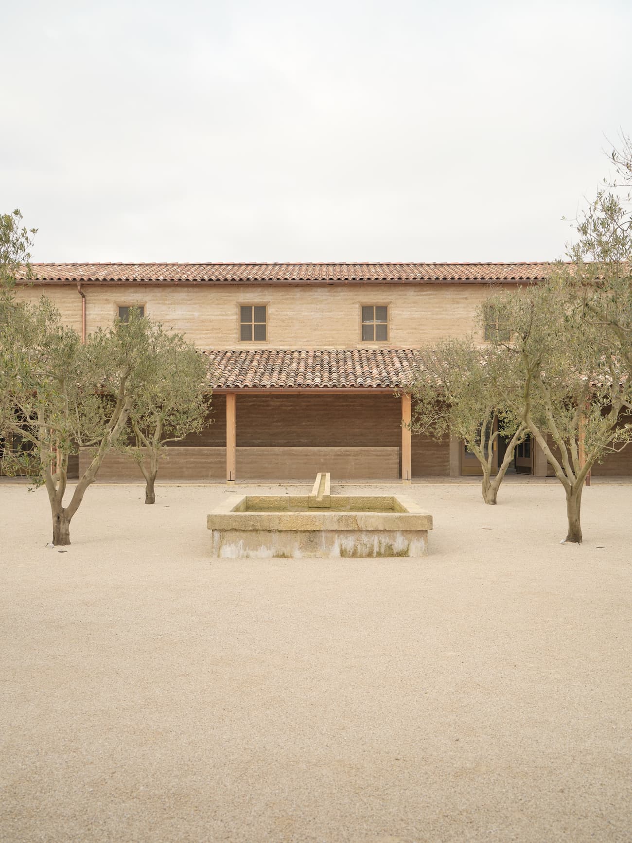 Architectural project - sturdy construction, tiled roof, minimalist landscape, terracotta roof, olive trees, Mediterranean courtyard, rustic house, mediterranean home, traditional facade, stone fountain, mediterranean architecture, pastoral environment, calming colors, harmonious setting, serene vibe, sustainable materials, outdoor space, natural light, outdoor living, eco friendly, farmhouse style, rustic charm, light brown, peaceful ambiance, neutral colors, tranquil setting, natural landscape, passive house, simple elegance, inviting entrance, beige tones, airy space, warm atmosphere, traditional design, classic architecture, exterior view, open air, gravel path, countryside house, textured facade, timeless design, plaster walls, simple lines, courtyard, rural retreat, clay tiles