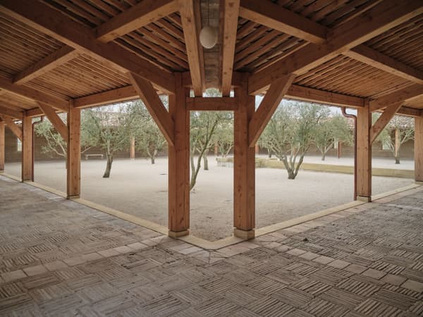 Architectural project - pergola, timber posts, shaded area, textured flooring, open courtyard, covered patio, earthy design, wood columns, natural landscaping, sandy ground, rustic flooring, semi-outdoor, natural materials, architectural design, wood, timber, relaxation area, outdoor space, natural light, outdoor living, sustainable design, warm tones, eco design, community space, exposed beams, timber structure, wooden ceiling, gathering space, beige, brown, light wood, eco friendly, timber beams, neutral palette, sand, wood structure, biophilic design, landscape integration, timber ceiling, rustic style, inviting space, warm atmosphere, rustic design, Mediterranean style, cozy outdoor, greenery, patio area, courtyard, trees