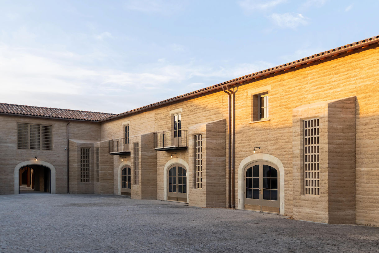 Architectural project - stone facade, beige facade, residential complex, historical restoration, rustic elegance, countryside vibe, cultural building, symmetrical design, historic preservation, arched windows, earthen walls, clay facade, open courtyard, communal courtyard, sunlit facade, timber windows, wooden windows, cobblestone path, clay architecture, Tuscan style, quiet setting, masonry, archways, eco-friendly design, sustainable materials, outdoor space, natural light, passive design, warm tones, community space, rustic charm, traditional building, serene atmosphere, rammed earth, rammed earth wall, energy efficient, traditional architecture, Mediterranean style, heritage building, exterior view, textured walls, rural charm, rustic exterior, craftsmanship, open space, natural insulation, courtyard, brown tones, earthy colors