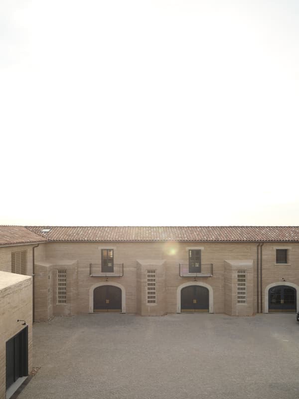 Architectural project - symmetrical layout, stone facade, balcony, light stone, heritage design, rustic courtyard, tan, arched windows, old-world charm, terracotta roof, classic design, traditional look, open courtyard, historical building, arched doors, double-story, second floor, front elevation, European architecture, timeless facade, solid construction, minimal design, serene vibe, calming atmosphere, outdoor space, natural light, warm tones, gathering space, beige, brown, rustic roof, sunlight, simple design, light tones, earth tones, stone, beige tones, clay, Mediterranean style, terracotta, stone wall, rural setting, countryside, exterior view, heritage architecture, timeless design, courtyard, clay tiles, texture contrast