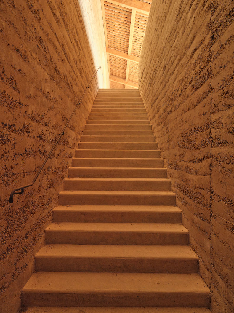 Architectural project - vertical lines, subtle elegance, low carbon materials, earth walls, earthy walls, outdoor steps, material contrast, natural walls, concrete stair, rustic stairs, rustic stairwell, softly lit, cosy space, rhythmic lines, pathway design, entrance design, tonal harmony, earth-inspired, cozy escape, minimal design, natural materials, architectural detail, eco-friendly design, sustainable materials, natural light, sustainable design, warm tones, exposed structure, daylight, light and shadow, simple design, rammed earth, raw texture, modern rustic, earthy tones, warm atmosphere, rustic ambiance, textured walls, earthy palette, stone steps, structural elements, warm lighting, welcoming space, tactile surfaces, earthy vibes