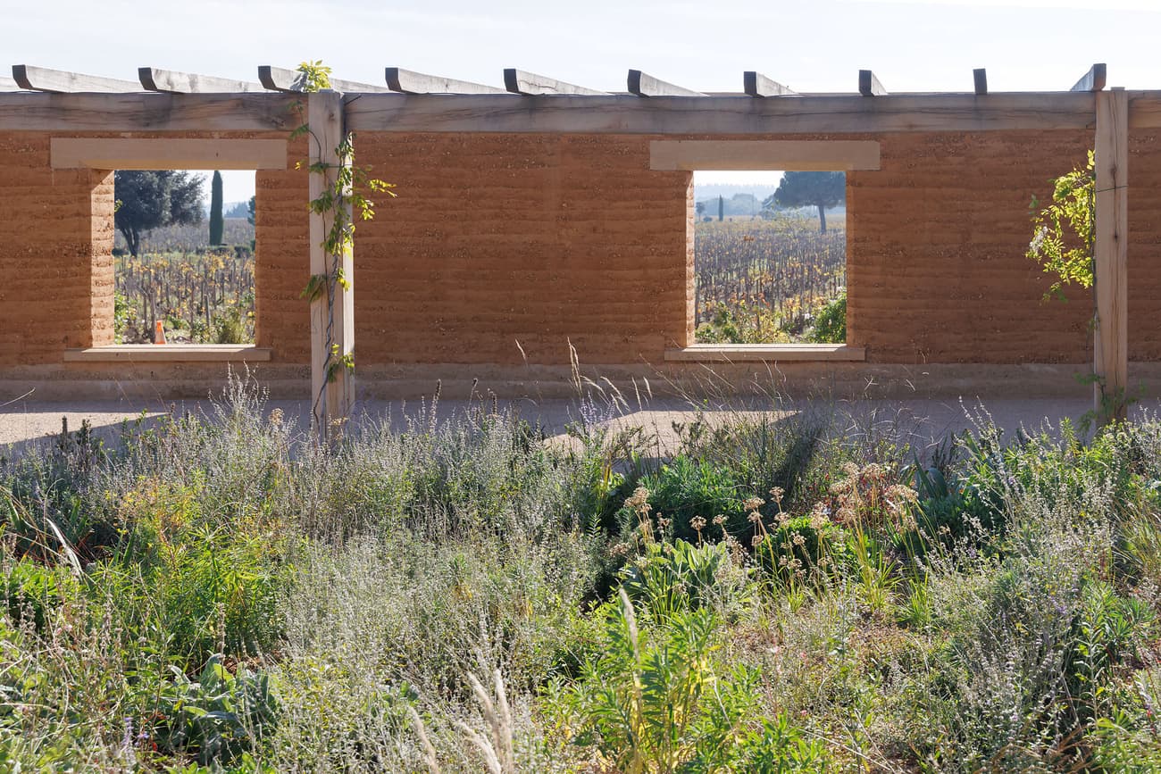 Architectural project - harmony with nature, native plants, garden architecture, pergola, wild garden, climate responsive, garden, clay walls, earth walls, countryside style, wooden pergola, vineyard view, green garden, white sky, rough finish, natural materials, wood, timber, raw materials, outdoor space, natural light, passive design, sustainable design, sustainable construction, work in progress, open frame, eco friendly, natural setting, rural architecture, blue sky, rammed earth, biophilic design, landscape view, beige color, earthy tones, rustic design, nature-inspired, organic materials, natural aesthetics, rustic architecture, natural wall, open air, eco architecture, earthy textures, nature blend, green plants