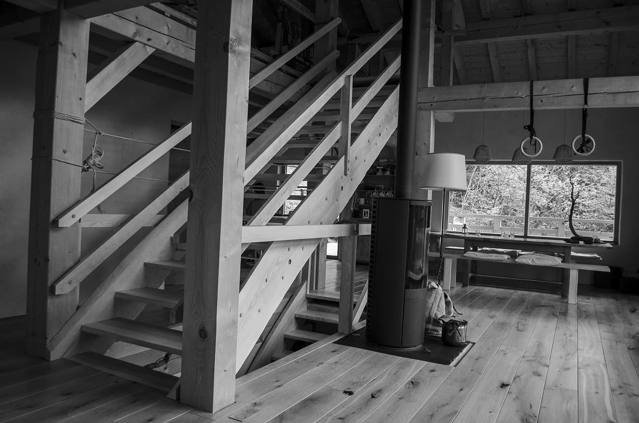 Architectural project - loft style, living room, fireplace, architectural beams, warm interior, natural materials, wood, timber, timber frame, relaxed vibe, natural light, warm tones, exposed beams, daylight, beige, brown, light wood, eco friendly, wooden beams, honey wood, rustic charm, timber floor, minimalist design, tranquil setting, sustainable home, passive house, indoor outdoor, Nordic style, large window, rustic style, wood cabin, cozy cabin, timber interior, open layout, inviting space, earthy tones, warm atmosphere, soft texture, countryside retreat, Scandinavian design, reading nook, lounge area, simple decor, wood flooring, wooden columns, staircase, living space