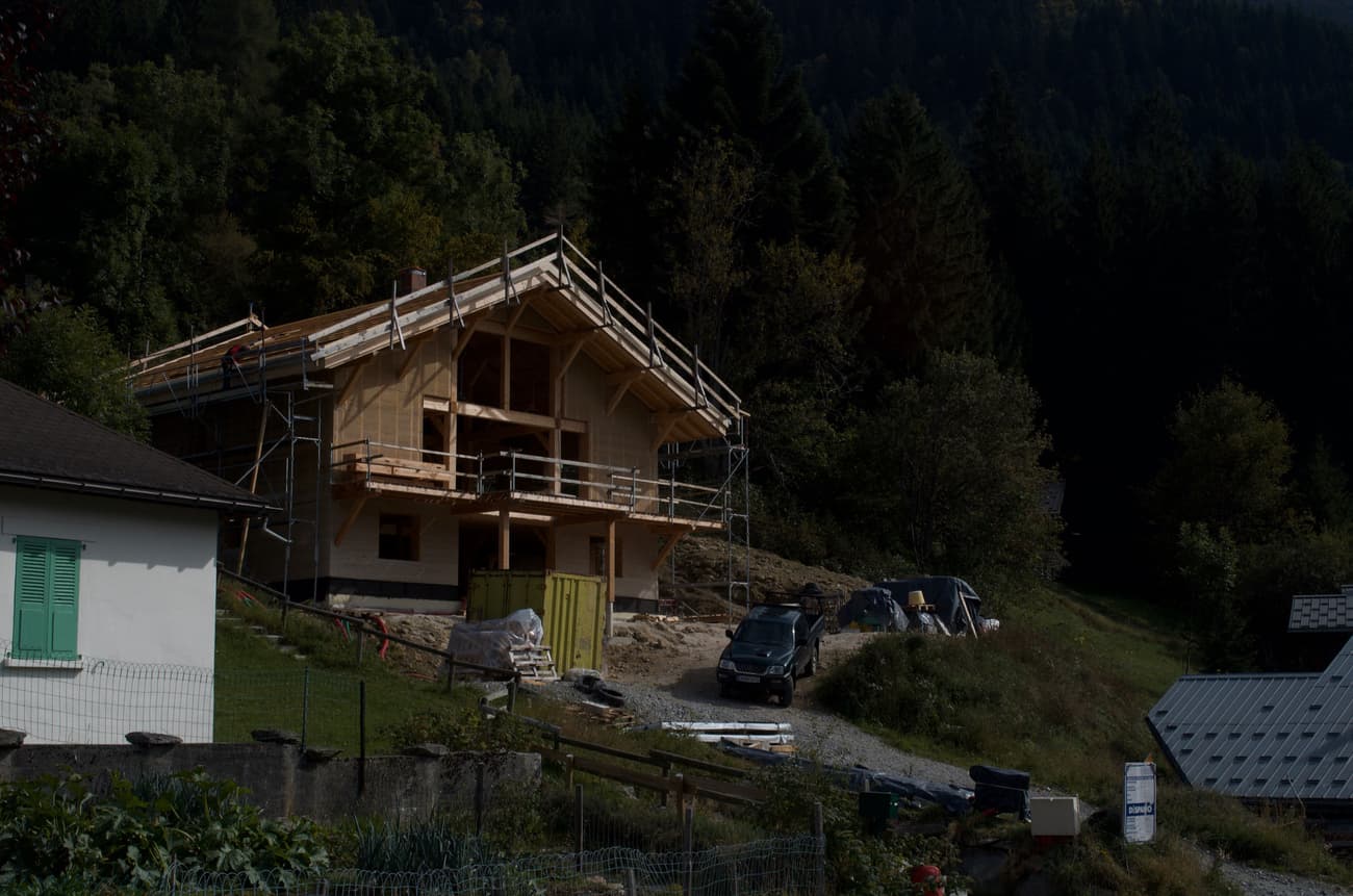 Architectural project - hillside view, forest backdrop, rural landscape, nature integrated, wooden balcony, traditional build, natural materials, wood, timber, scaffolding, outdoor living, passive design, exposed structure, green, construction site, under construction, brown, eco friendly, natural setting, timber construction, timber beams, rustic charm, serene atmosphere, sustainable building, eco home, hillside house, scenic view, wood cladding, cozy vibe, countryside home, natural colors, pitched roof, rustic design, rural setting, traditional style, gable roof, wooden facade, cabin style, rural retreat