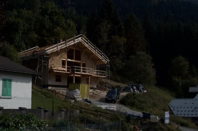 Architectural project - hillside view, forest backdrop, rural landscape, nature integrated, wooden balcony, traditional build, natural materials, wood, timber, scaffolding, outdoor living, passive design, exposed structure, green, construction site, under construction, brown, eco friendly, natural setting, timber construction, timber beams, rustic charm, serene atmosphere, sustainable building, eco home, hillside house, scenic view, wood cladding, cozy vibe, countryside home, natural colors, pitched roof, rustic design, rural setting, traditional style, gable roof, wooden facade, cabin style, rural retreat