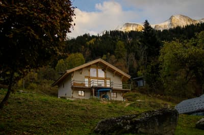 Architectural project - mountain retreat, forest backdrop, seasonal home, scenic location, rustic house, stucco, private getaway, wooden balcony, panoramic views, natural materials, wood, timber, natural light, outdoor living, passive design, warm tones, timber structure, beige, brown, wood beams, timber beams, cozy retreat, neutral palette, wood construction, natural landscape, earth tones, sustainable home, hillside house, large windows, inviting home, countryside home, stone, plaster, rural living, pitched roof, traditional design, tranquil atmosphere, gable roof, nature escape, serene setting, cottage style, cozy vibes, timber railing