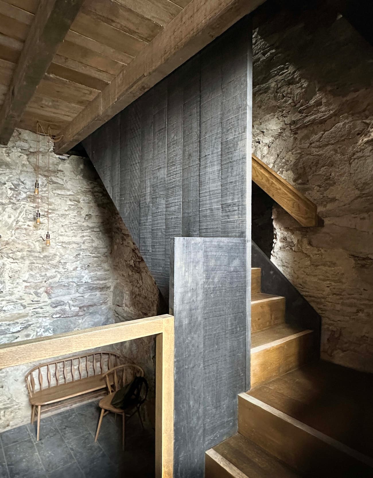 Architectural project - interior stair, exposed stone, rustic bench, rustic interior, vintage vibe, sitting area, pendant lights, reclaimed wood, loft vibe, ambient lighting, aged wood, staircase design, cottage charm, cozy interior, warm interior, natural materials, wooden bench, wood, timber, cottage feel, warm tones, grey, neutral tones, beige, brown, compact space, farmhouse style, simple design, rustic charm, minimalist design, raw texture, stone, small space, rough texture, stone wall, cozy corner, heritage building, traditional style, textured walls, grey stone, timber finish, vertical space, architectural feature, stairwell, wooden stair, timber stair, stone texture