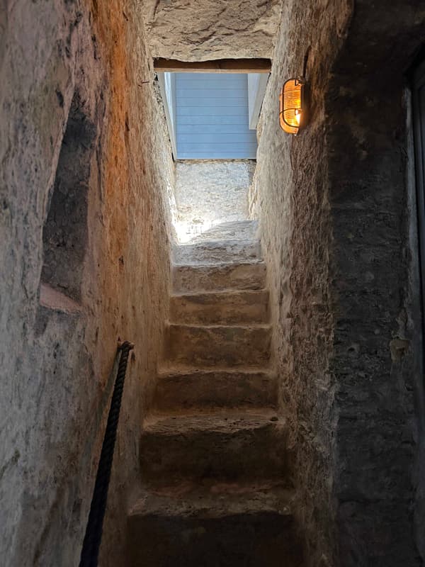 Architectural project - textured surfaces, minimal intervention, ambient light, stone walls, rustic, hidden gem, traditional construction, cozy lighting, enclosed space, dim lighting, heritage site, country style, underground vibe, stone material, handrail, historical architecture, pathway, quiet ambiance, natural materials, natural light, warm tones, beige, brown, compact space, rustic charm, rural design, stone, rough texture, earthy tones, textured walls, warm light, stone steps