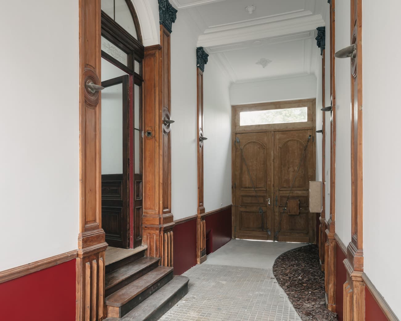 Architectural project - red walls, transitional space, welcoming atmosphere, historic building, period architecture, classic elegance, arched hallway, entrance hall, grand entrance, wood details, paneled door, tall door, vintage interior, classical style, classic charm, red paneling, decorative trim, ceiling moldings, period features, traditional aesthetics, inviting entry, ornate details, hallway steps, interior steps, stylish handles, decorative handle, rich textures, architectural character, old-world charm, statement hallway, historical vibe, transitional zone, indoor space, natural materials, wood, timber, warm tones, natural tones, neutral tones, beige, warm wood, elegant design, white, wood finishes, timber door, wooden door, red